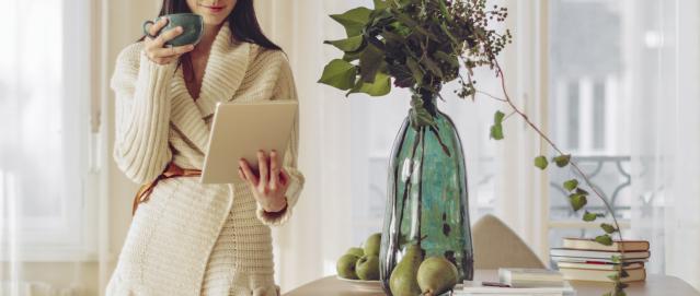 Woman drinking coffee looking at a tablet computer
