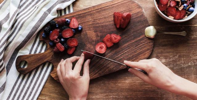 Woman's hands cutting berries on wood cutting board